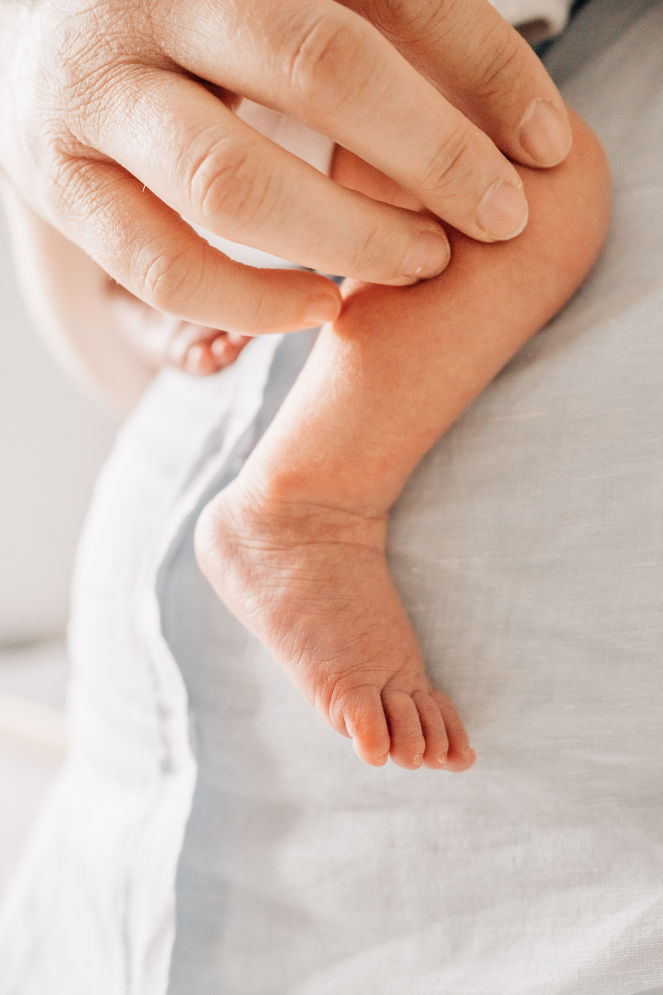 Newborn baby's leg and foot resting on mum's shirt, mum has her hand on the baby's leg